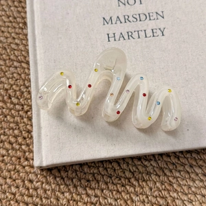 Close-up of cream wavy hair claw clip with colorful rhinestones on a textured background
