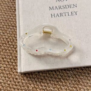 Detail of cream resin hair claw with colorful rhinestones and gold spring on a book