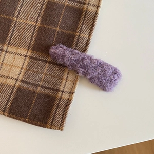 Close-up of a purple fuzzy plush hair clip on brown plaid fabric for winter styling