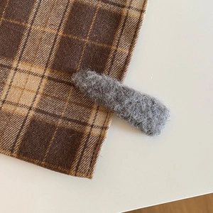 Close-up of a grey plush hair clip on checkered fabric, showing soft wool-like texture