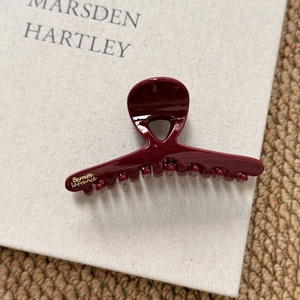 Detail showing deep red resin hair claw with golden Barrette LaFrance logo on a book