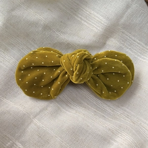 Detail of mustard yellow velvet bow hair clip with white polka dots on linen fabric