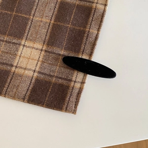 Close-up of black velvet oval hair clip showing the premium flocked texture on plaid fabric