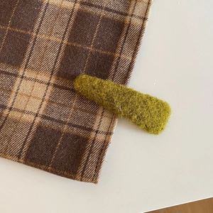 Close-up of soft moss green plush hair clip with fuzzy texture on brown checkered cloth