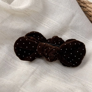Close-up of a brown velvet bow hair clip with white polka dots on soft linen fabric