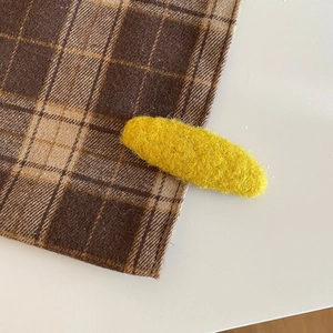 Detailed close-up of yellow plush oval hair clip with textured wool fabric surface