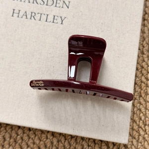 Close-up of wine red hair claw clip with gold glitter finish and logo on book background