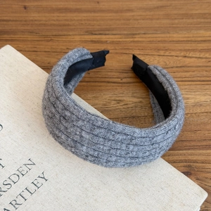Detailed close-up of grey cable-knit headband texture on a warm wooden background