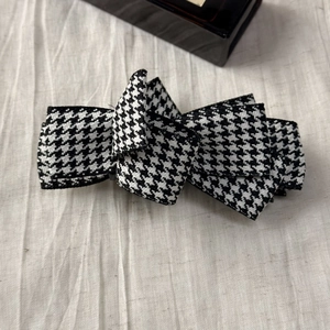 Macro detail of plaid bow hair clip showing black and white houndstooth fabric texture