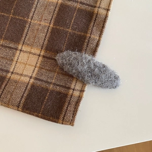 Detail shot of a grey plush oval hair clip textured with soft faux fur on plaid fabric