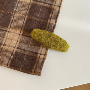 Detailed close-up of grass green wool felt oval hair clip on brown checkered fabric