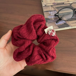 Détail du chouchou en tricot bordeaux avec texture torsadée et décor de cœur à carreaux