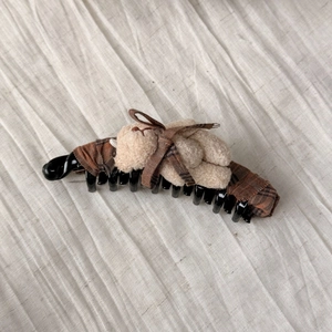 Detailed view of plush bear banana hair clip with brown plaid fabric on white texture