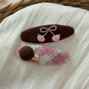 Détail d'un chouchou à carreaux et d'une pince à cheveux cerise brodée sur tissu blanc