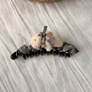 Detail view of a plaid fabric banana hair clip featuring a cute plush bear ornament
