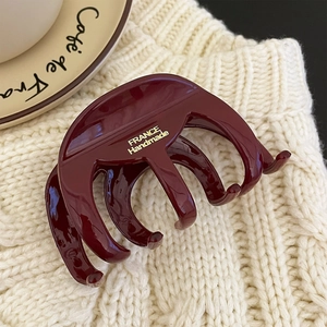 Close-up of glossy wine red hair claw clip with gold engraving on knit fabric