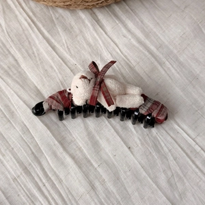 Detail of cute plush bear banana hair clip with red checkered bow on soft linen fabric