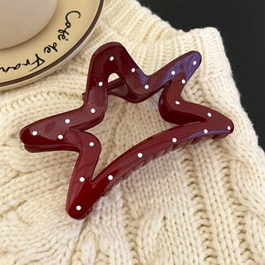 Macro detail of star-shaped red hair claw clip with white polka dots on cozy knit fabric