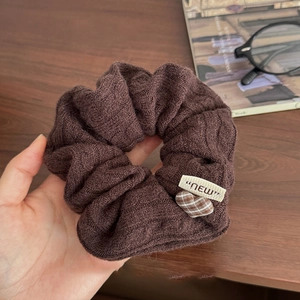 Détail d'un chouchou en tricot marron avec pendentif cœur à carreaux et petite étiquette