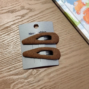 Close-up of a pair of brown fabric-wrapped drop hair clips on a warm wooden surface