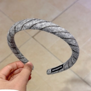 Detail of grey knitted headband with black diagonal stripes and handmade logo tag
