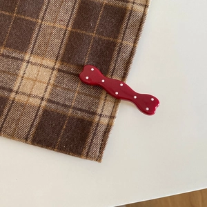 Detail shot of vintage red polka dot hairpin with a glossy finish on checkered fabric