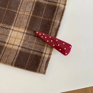 Close-up of a vintage red hair clip with white polka dots on a plaid background fabric