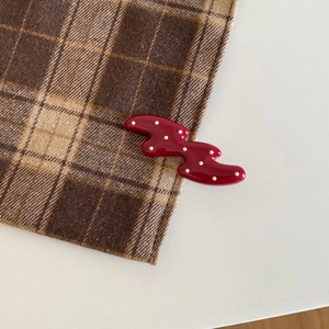 Macro detail of red wavy hair clip with white polka dots on brown plaid fabric