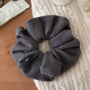 Détail du chouchou en maille gris foncé avec petite étiquette nœud sur tissu doux