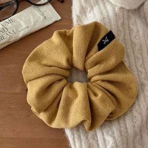 Détail d'un chouchou en tricot jaune moutarde avec une étiquette logo noire sur bois