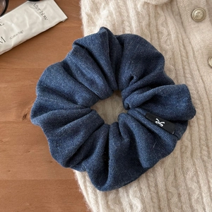 Détail de la texture d'un chouchou en denim bleu foncé sur un pull en maille