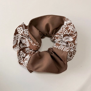 Gros plan sur chouchou marron avec broderie florale blanche et texture en coton