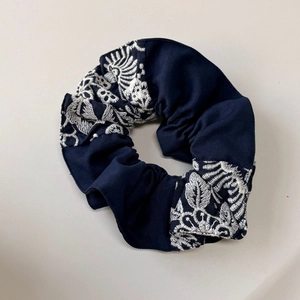 Détail d'un chouchou bleu foncé avec broderie florale blanche et texture en tissu de coton