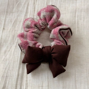 Détail d'un chouchou à carreaux rose et gris avec un nœud brun sur fond de lin