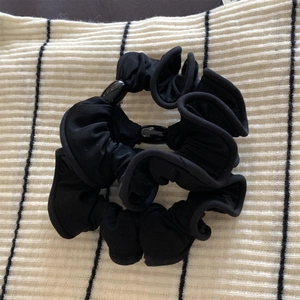 Détail d'un chouchou noir plissé avec deux perles brillantes sur fond rayé noir et blanc