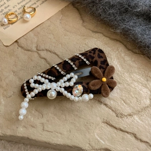 Elegant leopard print hair clip with pearls and brown velvet flower detail on stone surface