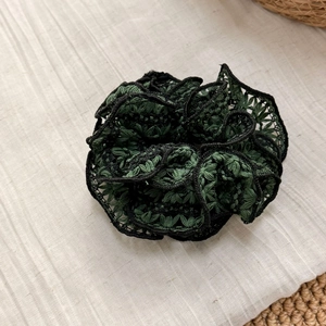 Detail of woven lace scrunchie with dark green floral embroidery and ruffled black edges