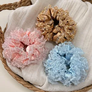 Three satin and sequined lace scrunchies in pink, champagne, and sky blue in a basket