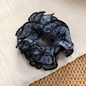 Detailed macro view of woven blue lace scrunchie with intricate embroidery and black edging