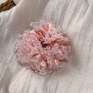 Close-up of pink satin scrunchie with lace edges and sequins on soft beige fabric