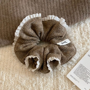Macro detail of brown knit scrunchie with white lace edges and branded woven logo