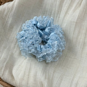 Close-up of light blue satin scrunchie with layered lace edges and iridescent sequins