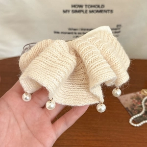 Détail d'une pince à cheveux en tricot crème avec volants et perles blanches suspendues