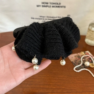 Détail d'une pince à cheveux noire tricotée avec des perles blanches suspendues