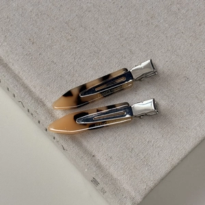 Detail view of two tortoise shell hair clips with silver metal grip and handmade texture