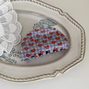 Macro detail of cherry plaid hair claw clip on a vintage ceramic tray with white lace