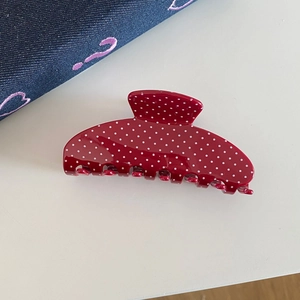 Macro detail of red hair claw clip with white polka dots on denim background