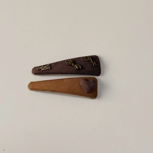 Detail of two handmade fabric hair clips in brown and camel with metal bow and heart