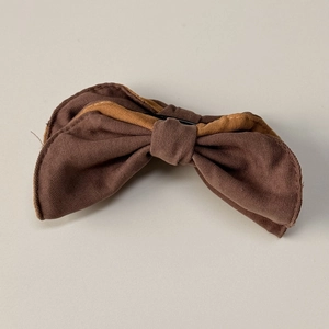Detail of a brown bow hair clip showing twill fabric texture and dual-tone stitching