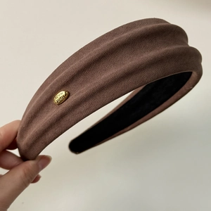 Detail of a brown fabric headband with a golden metal tag and non-slip lining